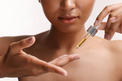 Woman applying serum onto her finger on white background, closeup