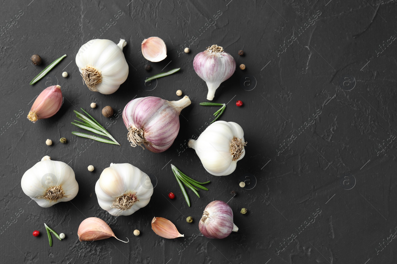 Photo of Fresh garlic, rosemary and peppercorns on dark textured table, flat lay. Space for text