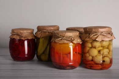 Photo of Many jars with preserved vegetables on white wooden table