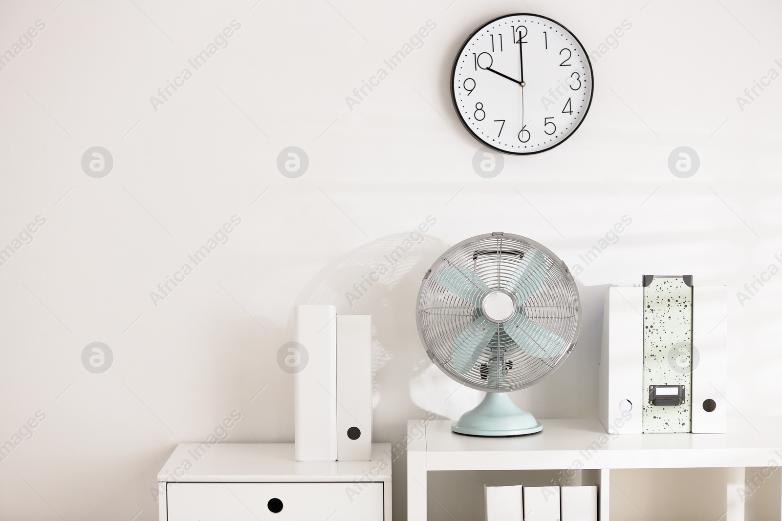 Photo of Modern electric fan on shelving unit in office. Space for text