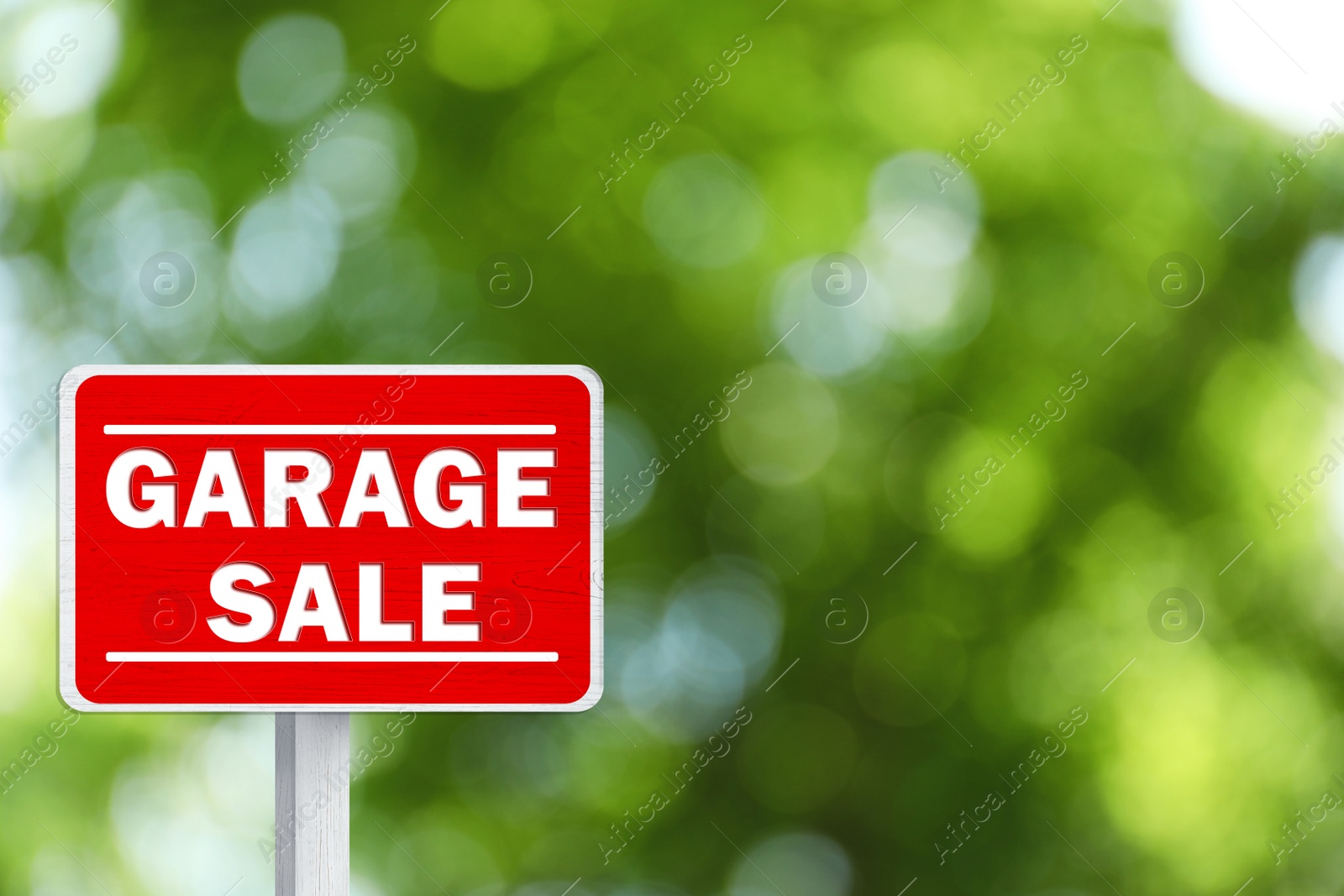 Image of Sign with phrase GARAGE SALE on blurred green background, bokeh effect