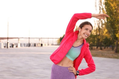 Photo of Young woman with wireless headphones listening to music while exercising outdoors. Space for text