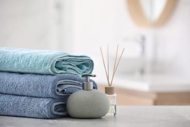 Stack of fresh towels, reed air freshener and soap dispenser on table in bathroom