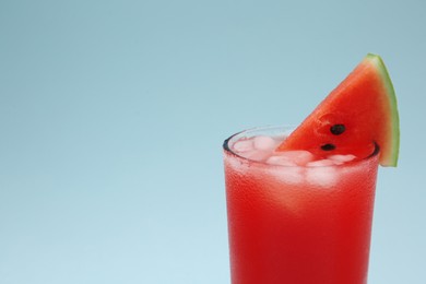 Delicious drink with ice cubes and piece of fresh watermelon on light blue background, closeup. Space for text