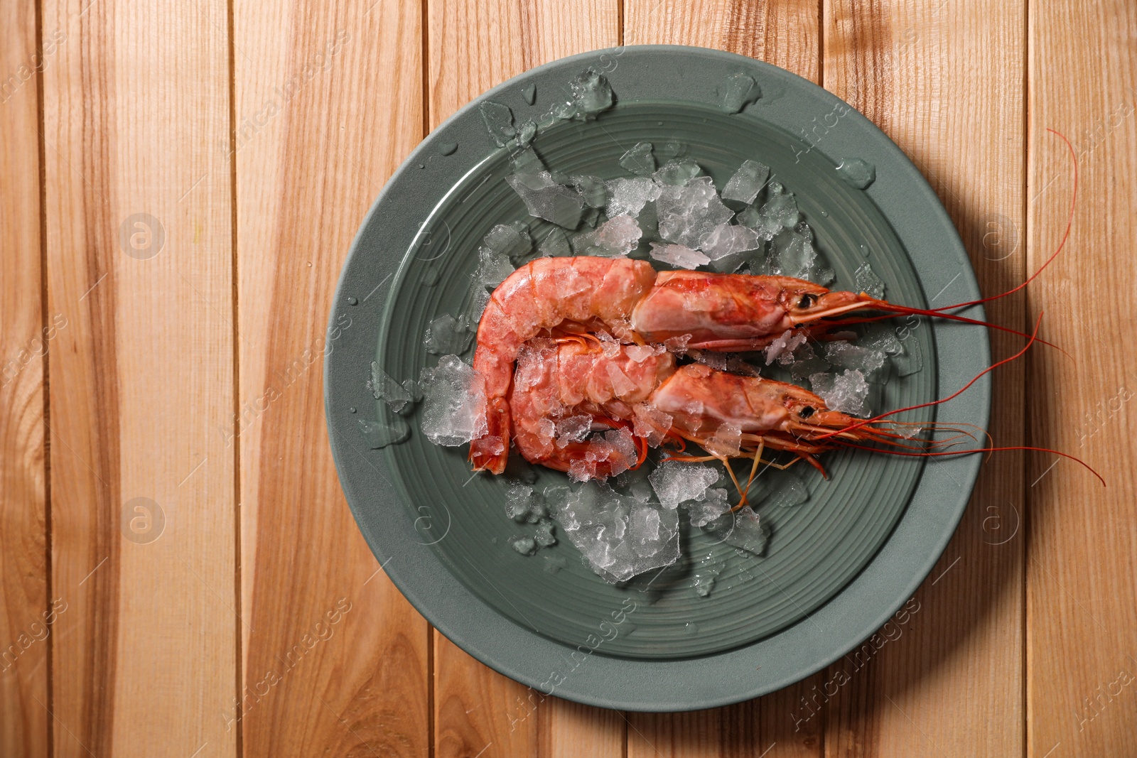Photo of Fresh royal shrimps with ice on wooden table, top view