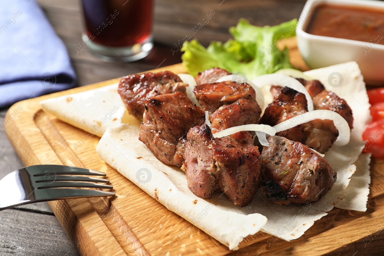 Photo of Wooden board with juicy shish kebab, closeup