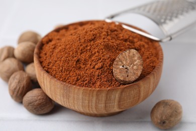 Photo of Nutmeg powder in bowl and seeds on white table, closeup