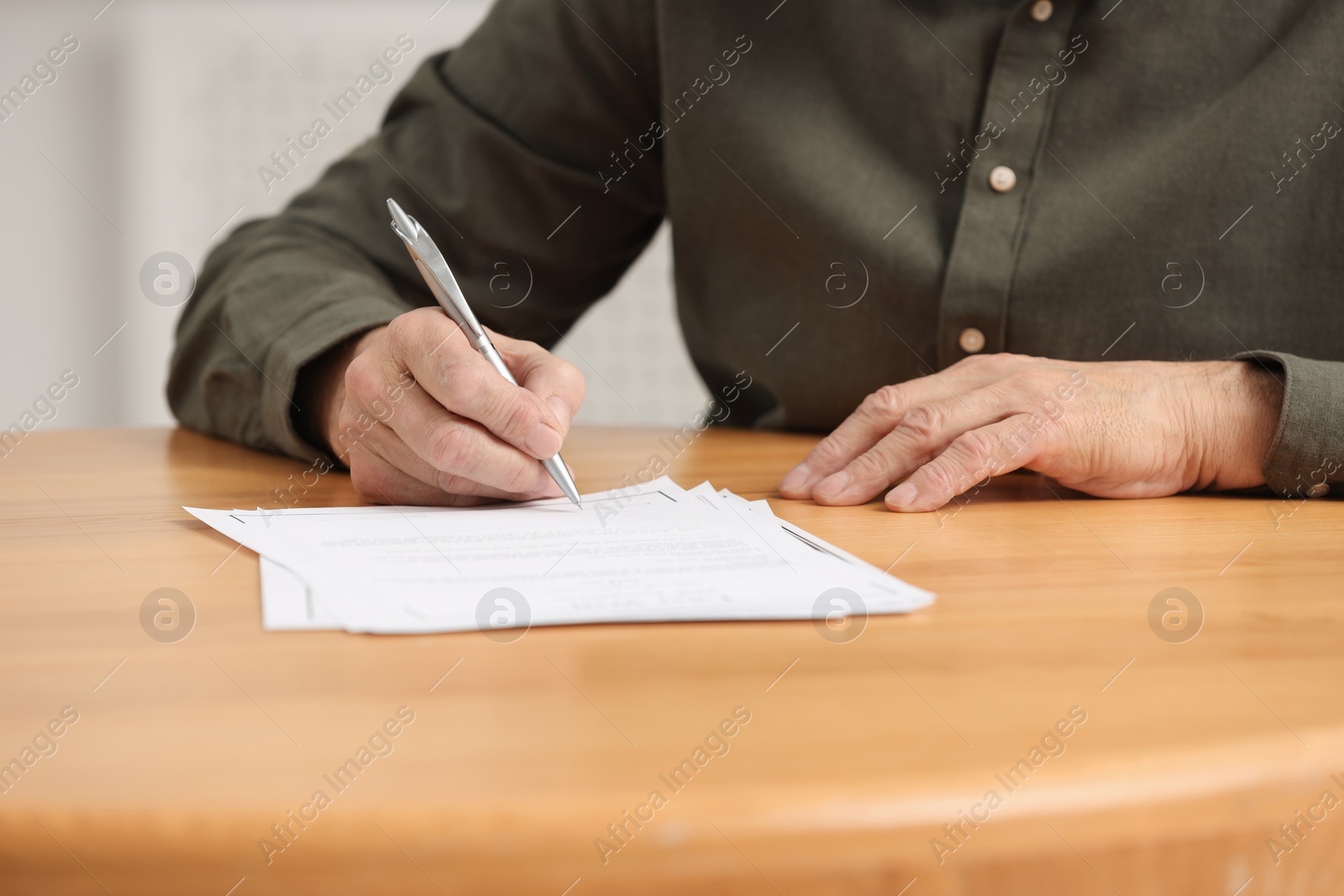 Photo of Senior man signing Last Will and Testament at wooden table indoors, closeup