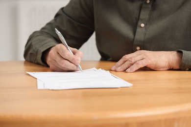 Senior man signing Last Will and Testament at wooden table indoors, closeup