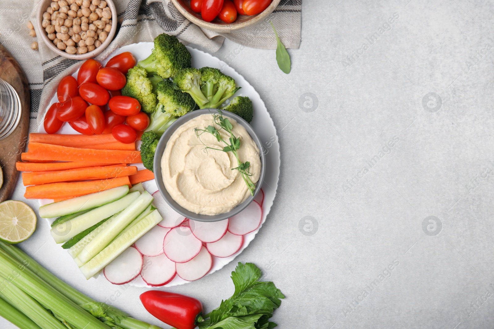 Photo of Plate with delicious hummus and fresh vegetables on light grey table, flat lay
