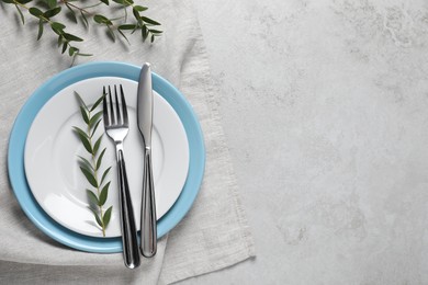 Stylish setting with cutlery and eucalyptus leaves on light grey table, flat lay. Space for text