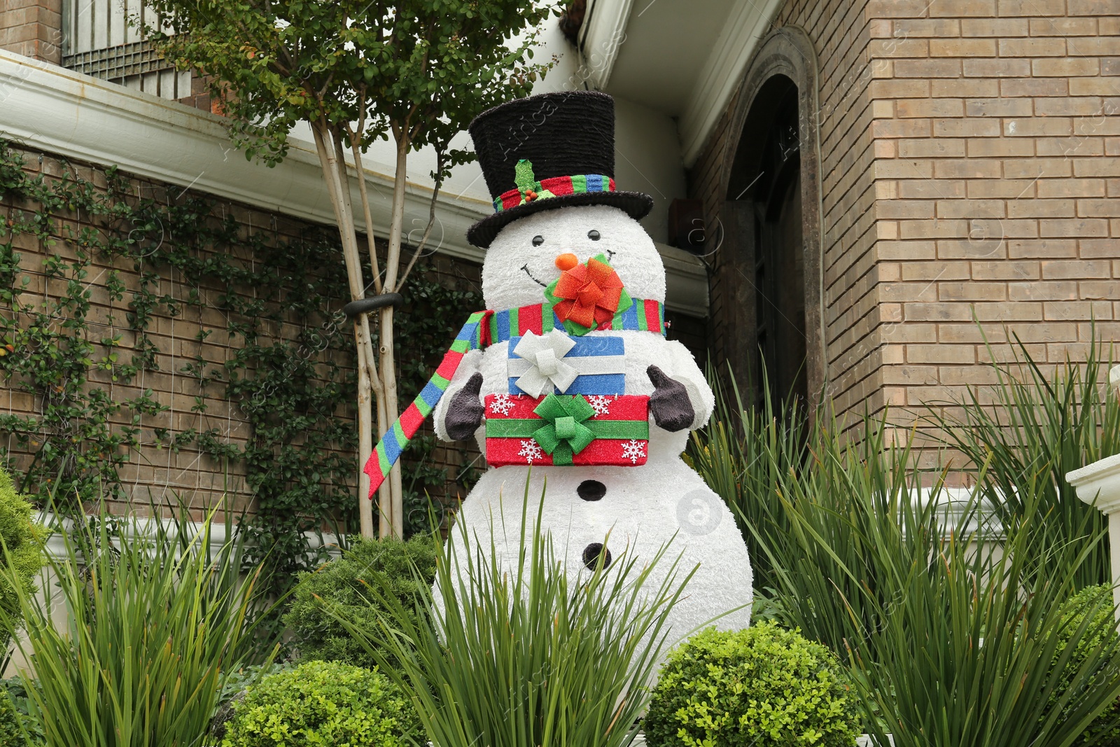 Photo of Funny snowman near house outdoors. Festive Christmas decoration