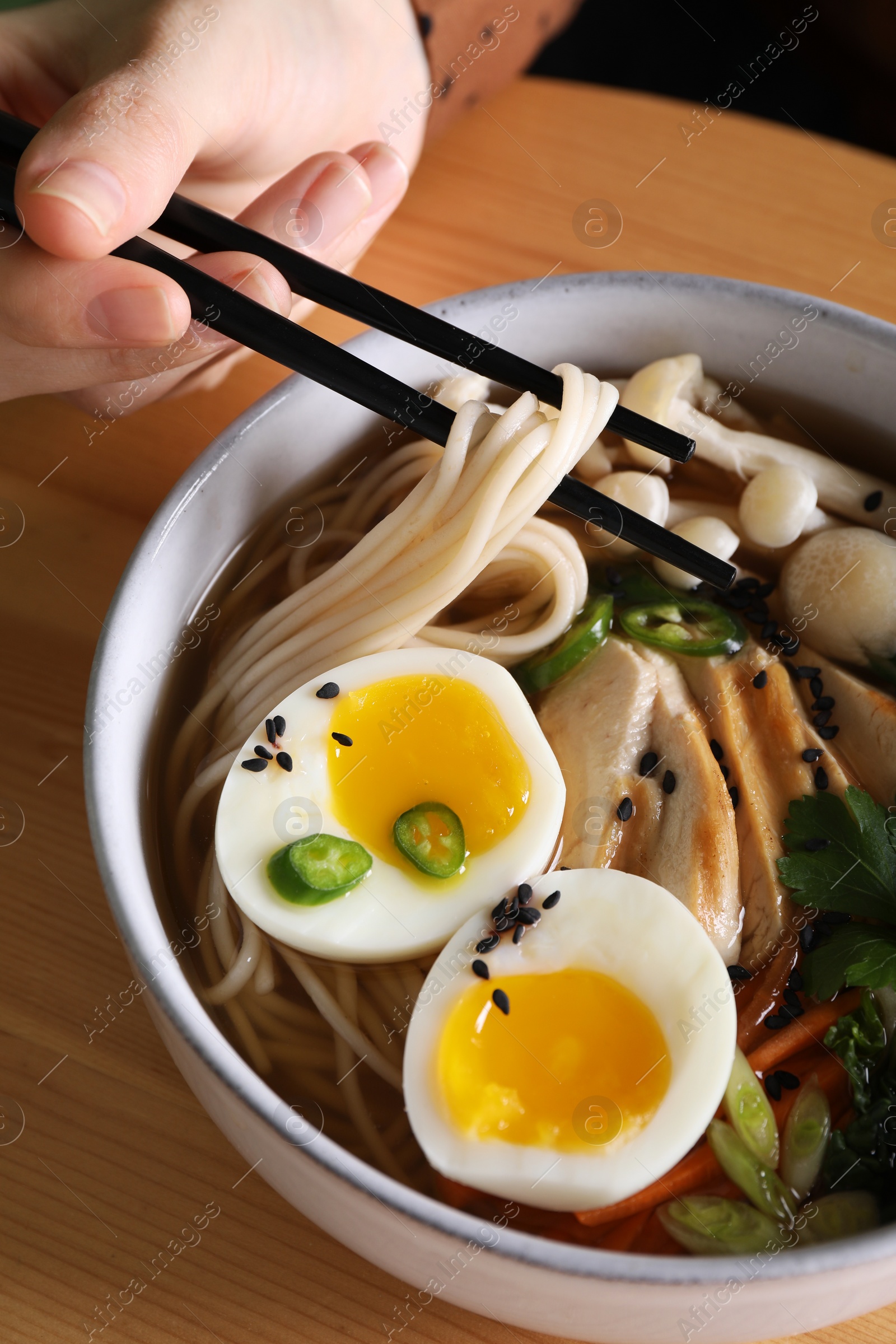 Photo of Woman eating delicious ramen with chopsticks at wooden table, closeup. Noodle soup