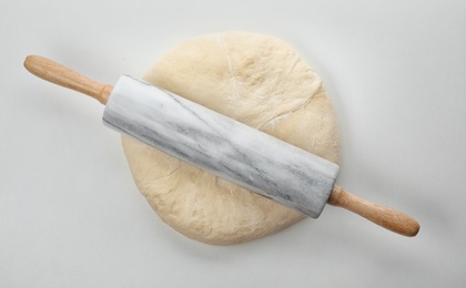 Photo of Raw wheat dough and rolling pin on white background, top view