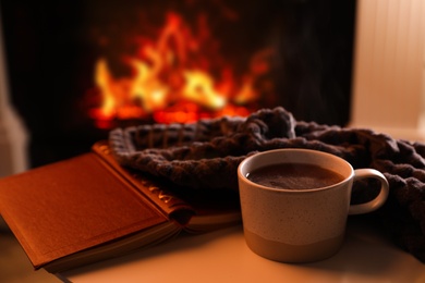Cup of hot drink and book on table near fireplace indoors