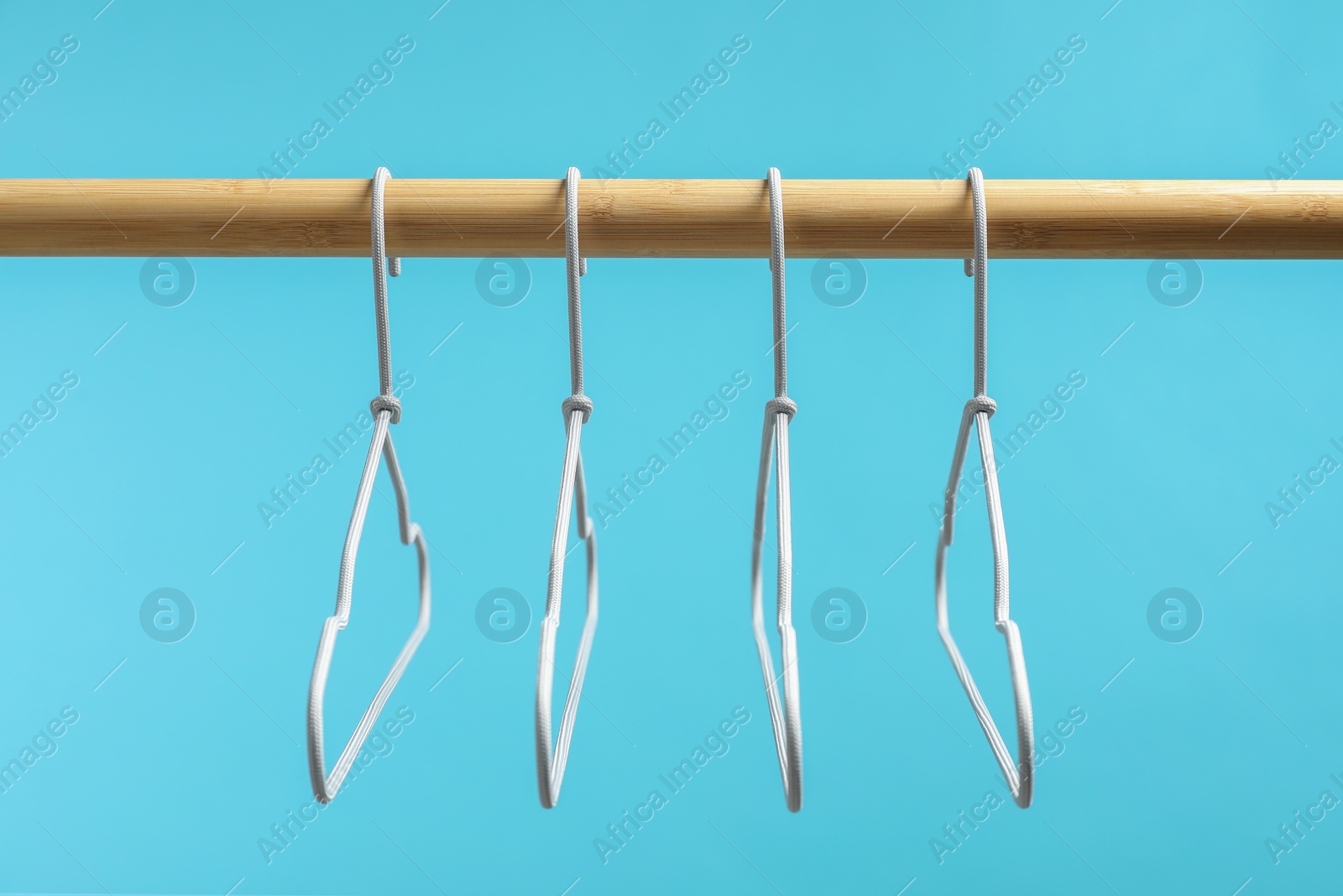 Photo of Empty clothes hangers on wooden rack against light blue background