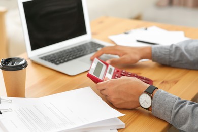 Man working with calculator at wooden table in office, closeup