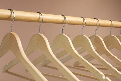 Photo of Empty clothes hangers on wooden rack against light brown background, closeup