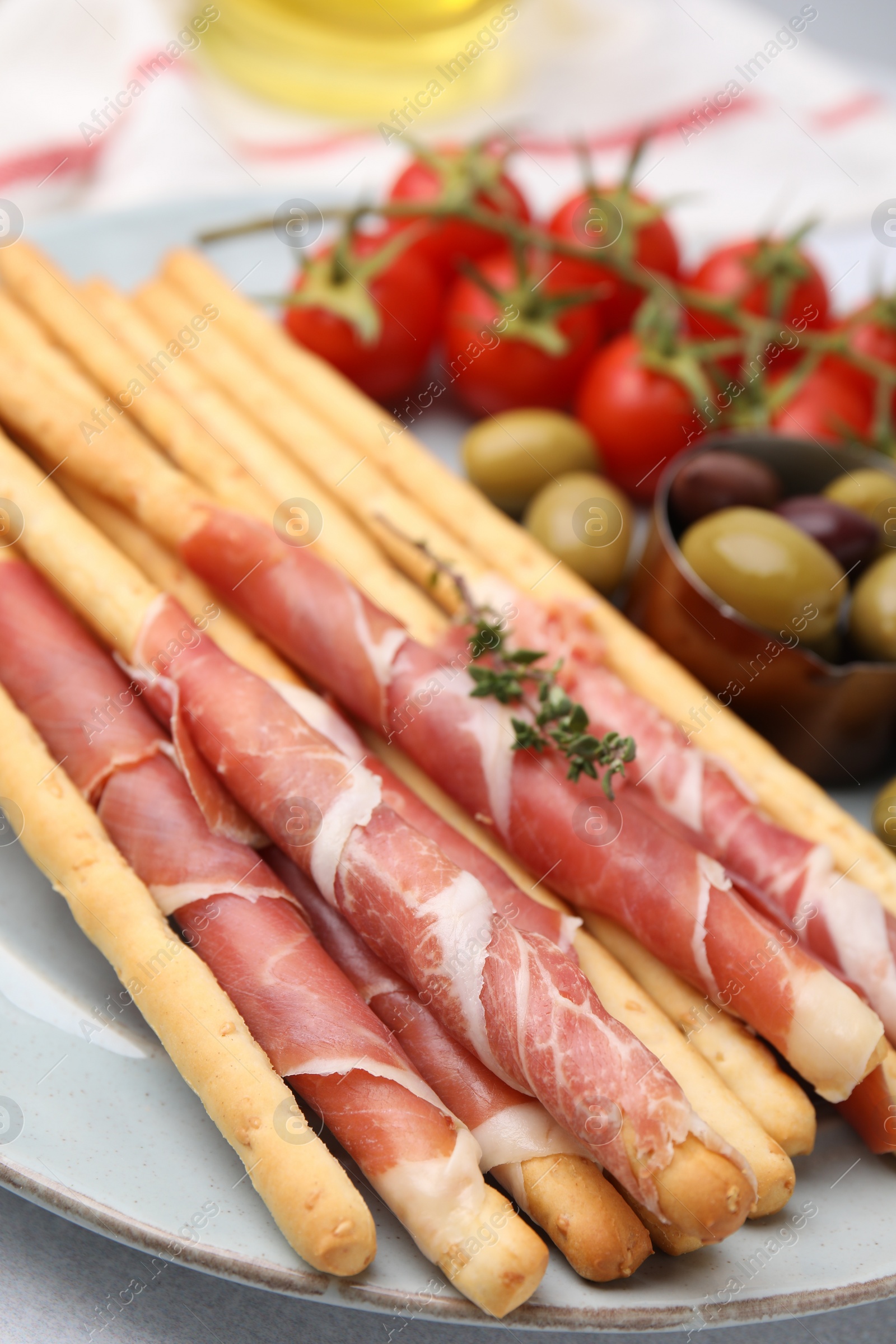 Photo of Delicious grissini sticks with prosciutto and snacks on white table, closeup