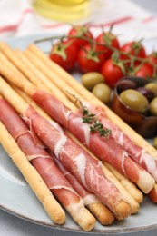 Delicious grissini sticks with prosciutto and snacks on white table, closeup
