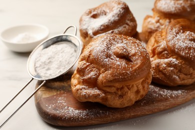 Photo of Delicious profiteroles with powdered sugar on wooden board, closeup