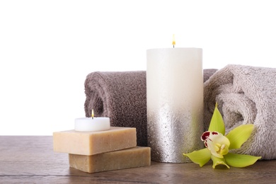 Composition with towels, candle and soap bars on wooden table against white background