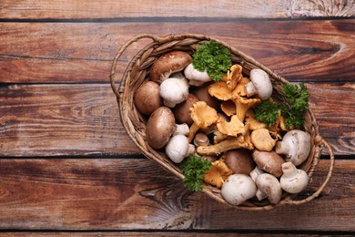 Photo of Basket with different mushrooms on wooden table, top view. Space for text
