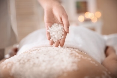 Beautiful young woman having massage with body scrub in spa salon