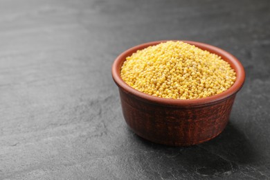 Photo of Millet groats in bowl on black table, space for text