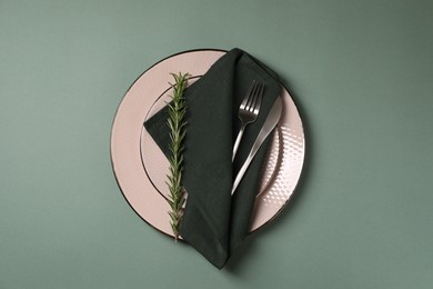 Stylish table setting. Plates, cutlery, napkin and rosemary on green background, top view