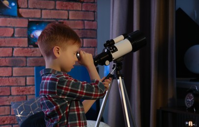 Little boy looking at stars through telescope in room