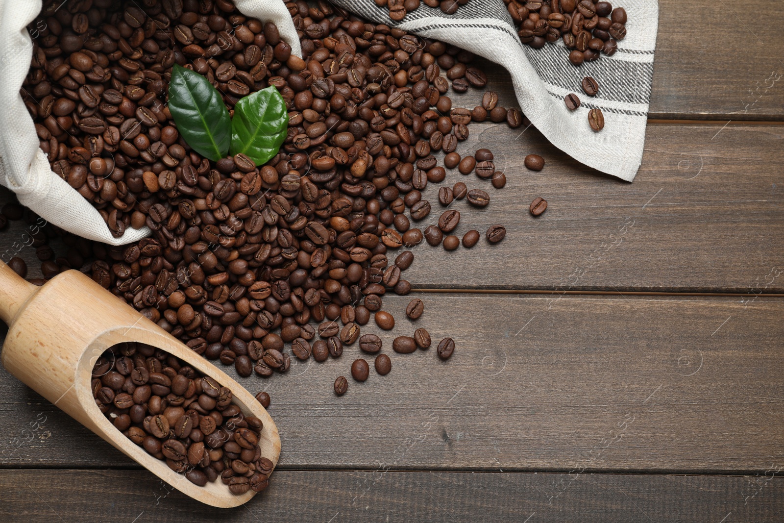 Photo of Scoop and bag with roasted coffee beans on wooden table, flat lay. Space for text