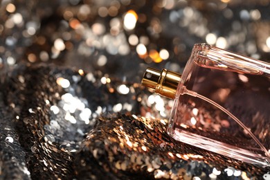 Luxury perfume in bottle on fabric with shiny sequins, closeup