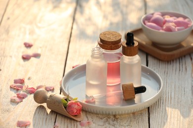 Photo of Bottles of rose essential oil and flowers on white wooden table, space for text