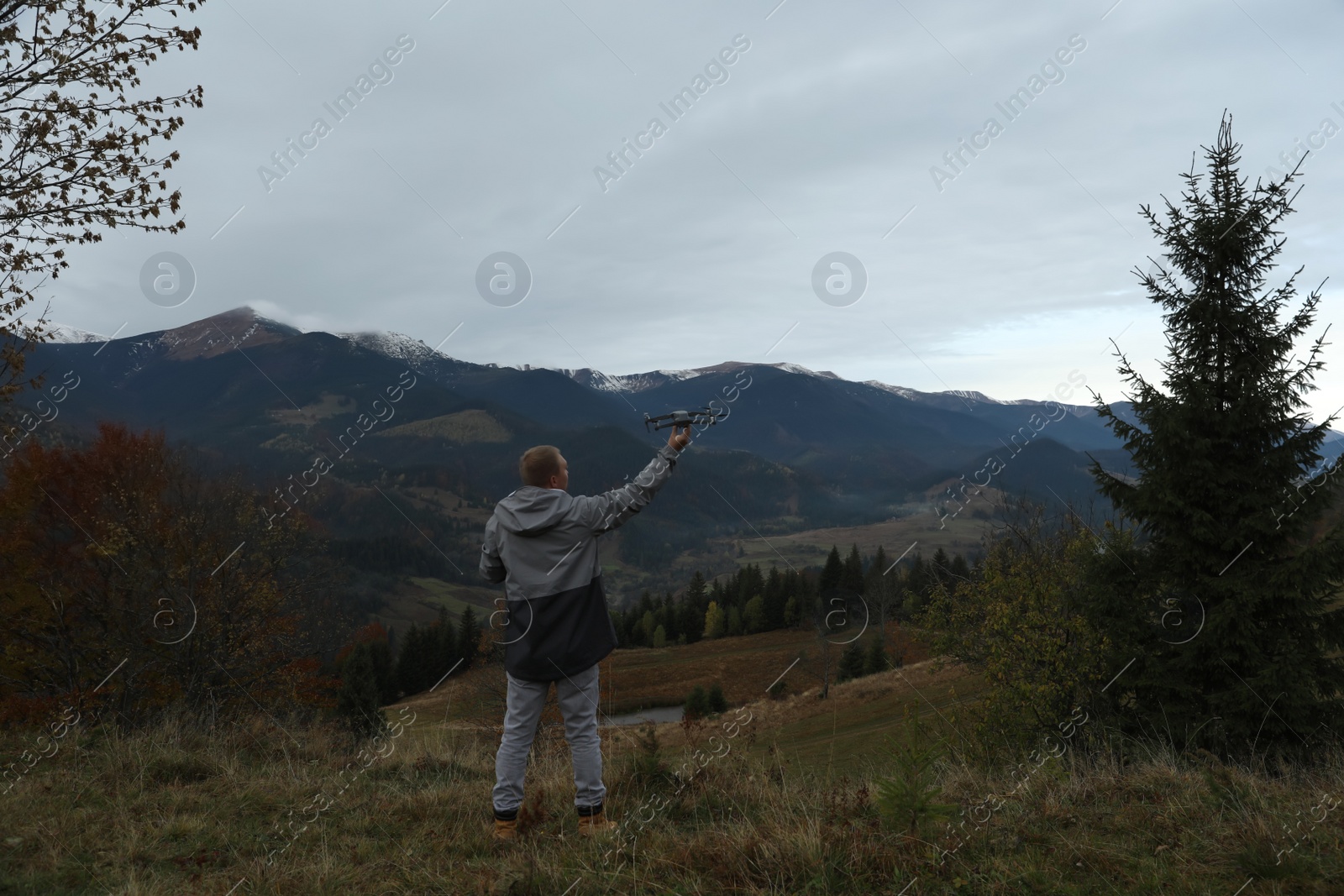 Photo of Young man with modern drone in mountains, back view