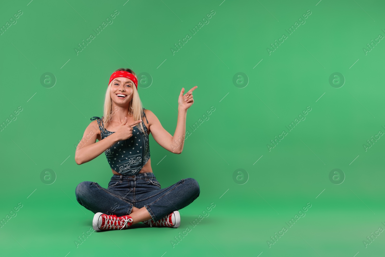 Photo of Portrait of happy hippie woman pointing at something on green background. Space for text