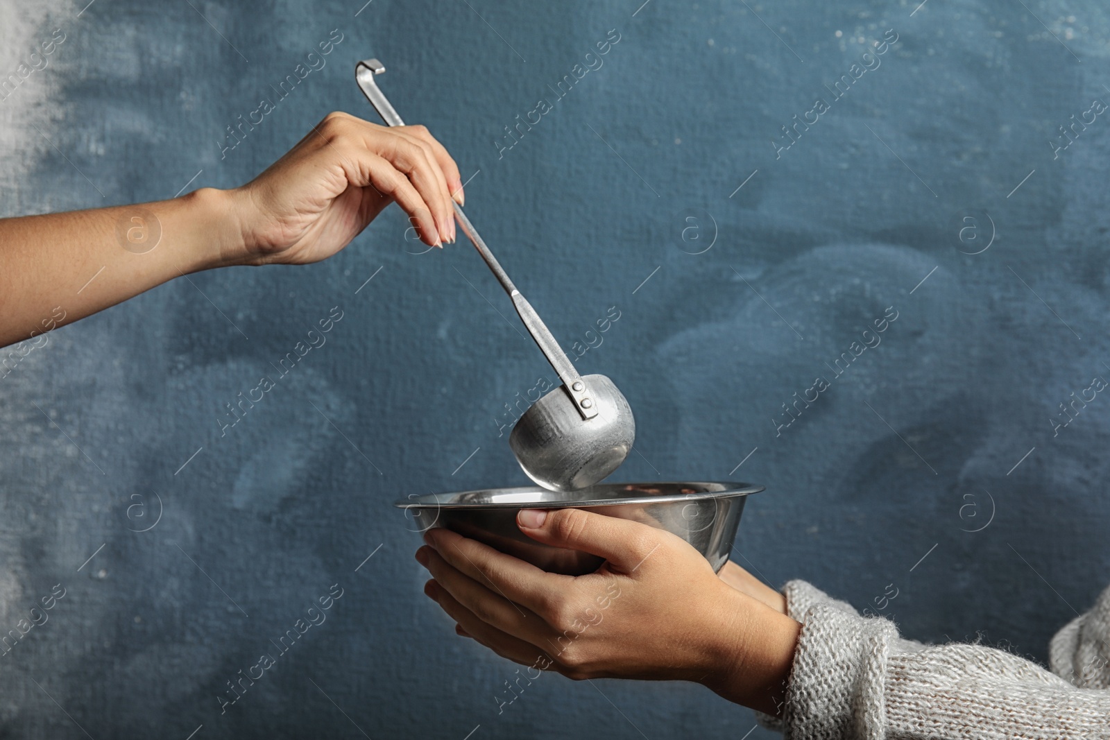 Photo of Volunteer putting food into bowl of poor woman on color background, closeup. Concept of help