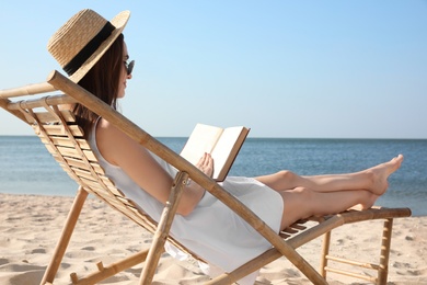 Young woman reading book in deck chair on beach