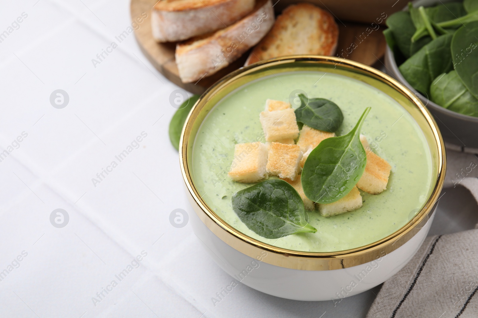 Photo of Delicious spinach cream soup with croutons in bowl on white tiled table. Space for text