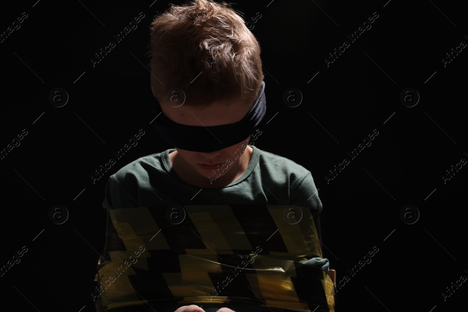 Photo of Blindfolded little boy tied up and taken hostage against dark background