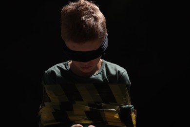 Blindfolded little boy tied up and taken hostage against dark background