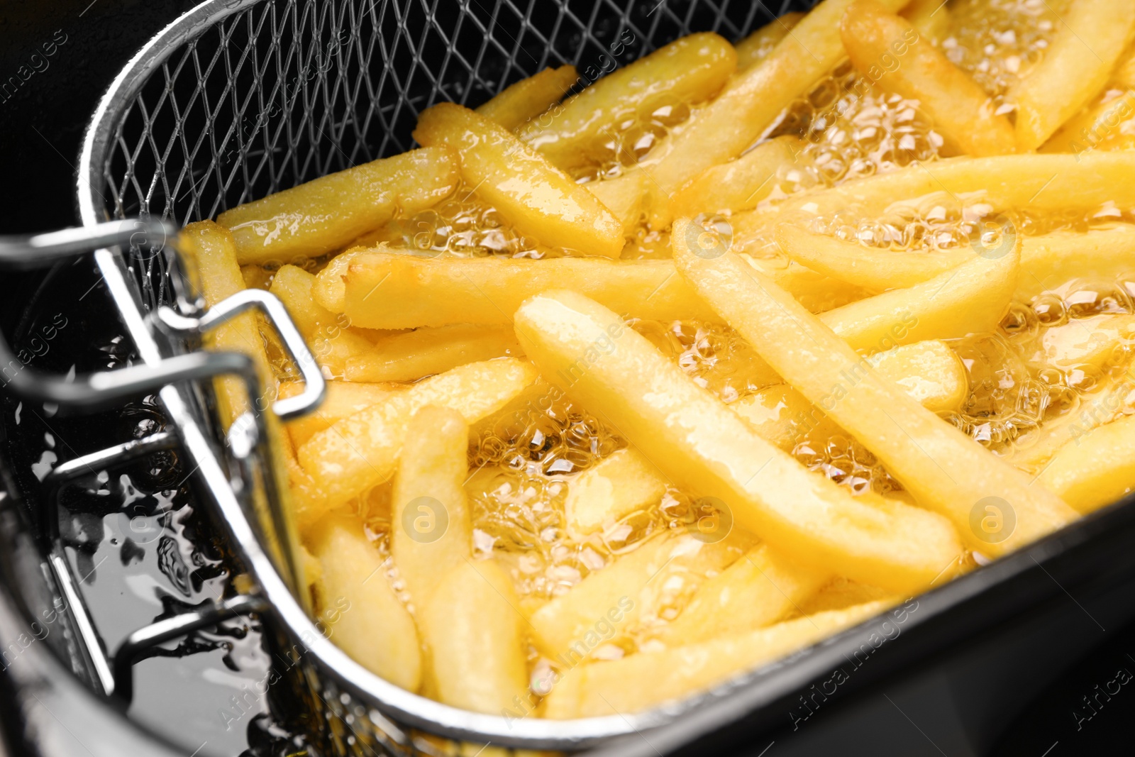 Photo of Cooking delicious french fries in hot oil, closeup