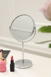 Mirror, cosmetic products and pink roses on white dressing table, closeup