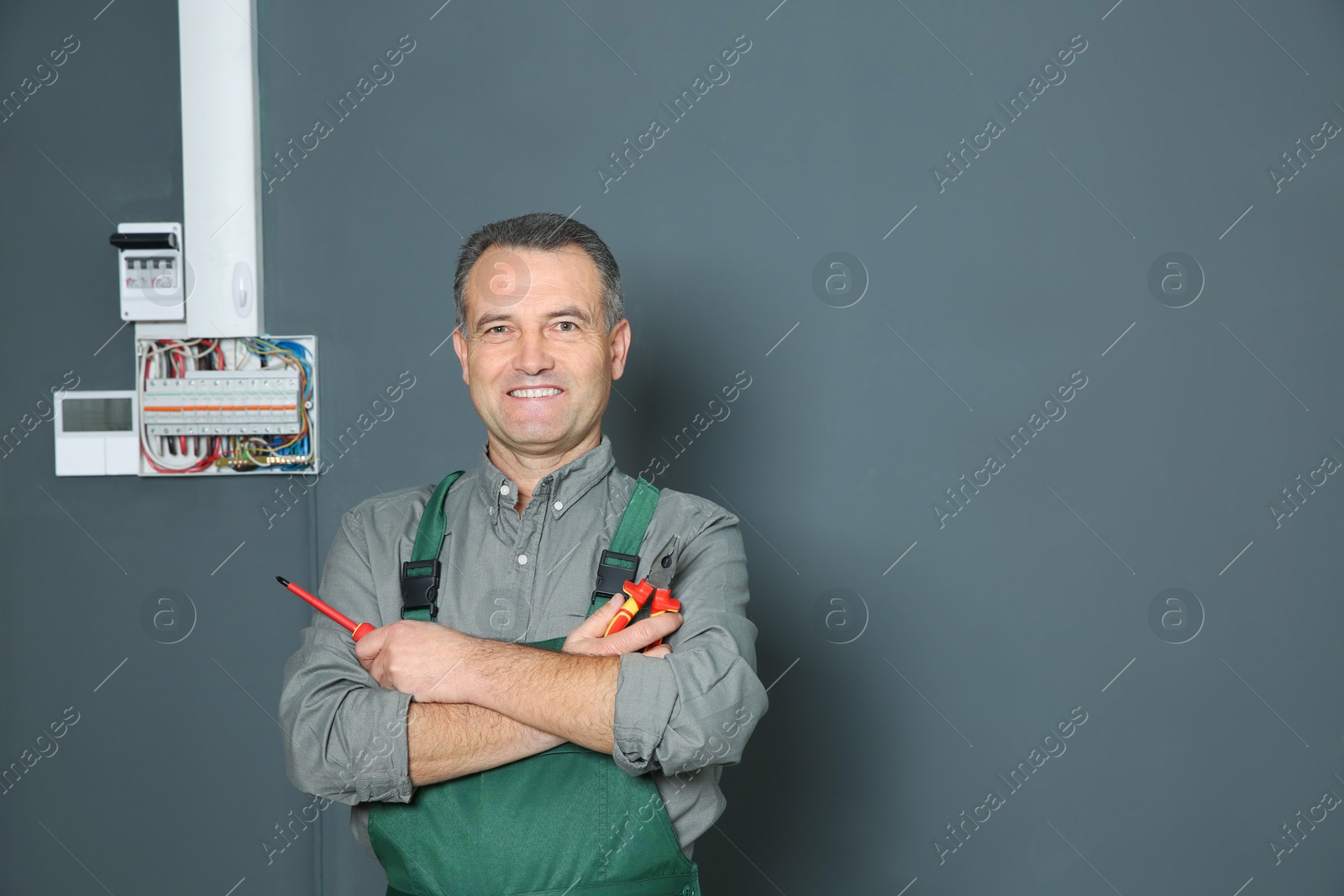 Photo of Electrician with instruments standing near fuse board on grey wall, space for text