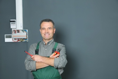 Photo of Electrician with instruments standing near fuse board on grey wall, space for text