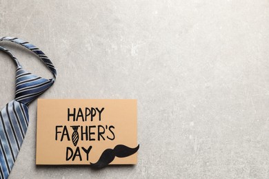 Card with phrase Happy Father's Day, paper mustache and necktie on light grey background, flat lay. Space for text