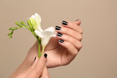 Woman with black manicure holding flower on color background, closeup. Nail polish trends