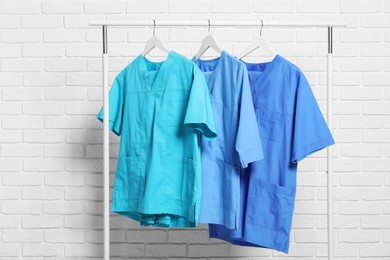 Photo of Medical uniforms hanging on rack near white brick wall