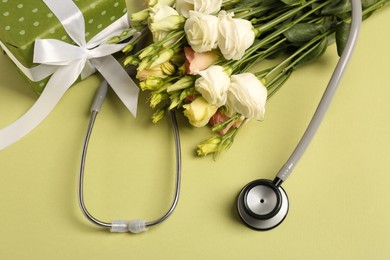 Photo of Stethoscope, gift box and flowers on green background, above view. Happy Doctor's Day