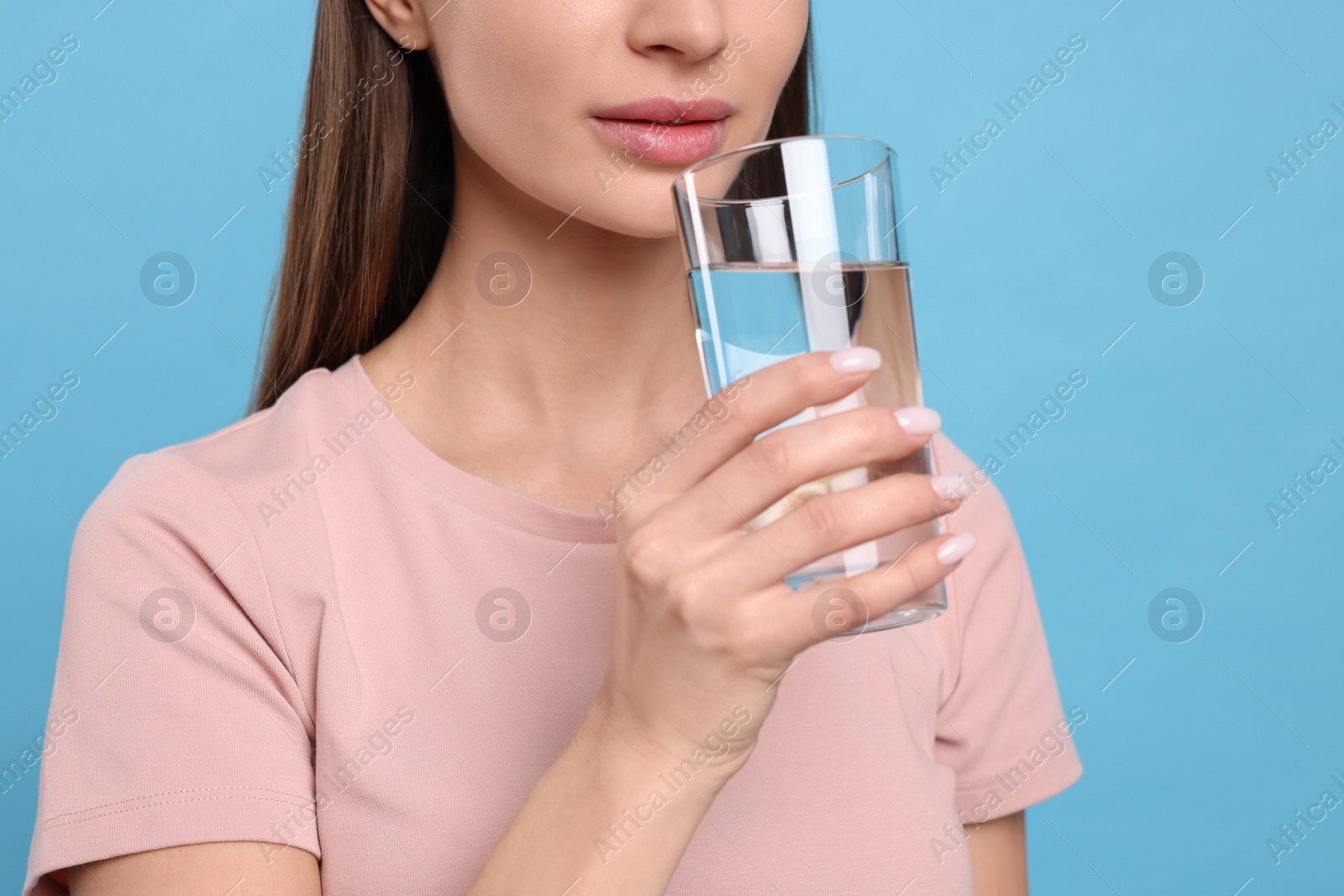 Photo of Healthy habit. Woman drinking fresh water from glass on light blue background, closeup